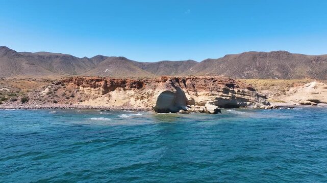 Low flight close up to rugged volcanic shoreline of La Isleta del Moro Spain