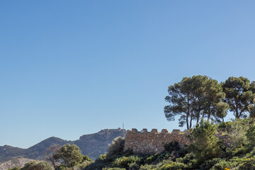 Obraz premium The ancient stone wall of Roman-era fortresses in Cartagena, Spain, rises majestically against the backdrop of a rugged mountain, the historic strength and enduring beauty
