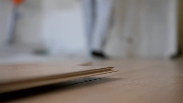 Detailed close-up of laminate plank lock connection during floor installation in apartment renovation. Focus on precise fitting of flooring panels.