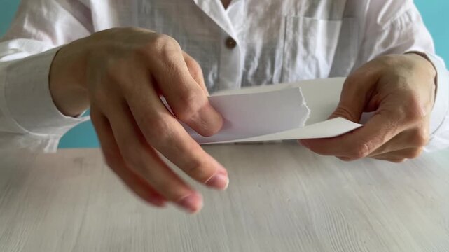 close-up of human hands ripping white paper into pieces on a table,sharp tear texture and realistic paper ripping audio,concept of stress relief,breakup,or disposal