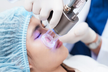 Naklejka premium Detailed aesthetic clinic scene showing Asian patient relaxed with eyes closed during facial laser therapy, symbolizing anti aging treatment, medical beauty service, and high technology skincare.