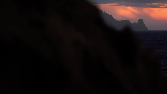 Cinematic reveal of Es Vedra at sunset in Ibiza as camera moves from behind rock to show island silhouette over Mediterranean sea.