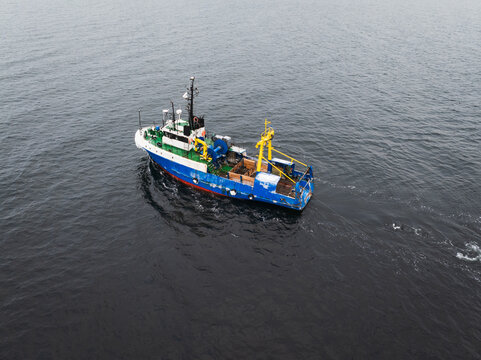Aerial drone view of a blue commercial fishing vessel trawling nets in the deep waters of the Baltic Sea during winter.