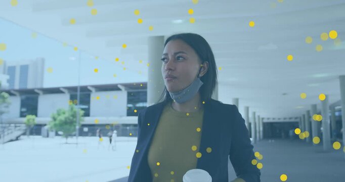 Animation of yellow spots floating over african american woman holding coffee cup walking at office