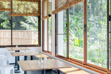 Fototapeta premium Minimalist Japanese Cafe Interior with Wooden Tables and Bamboo Blinds Overlooking Green Nature for Tranquility and Peace