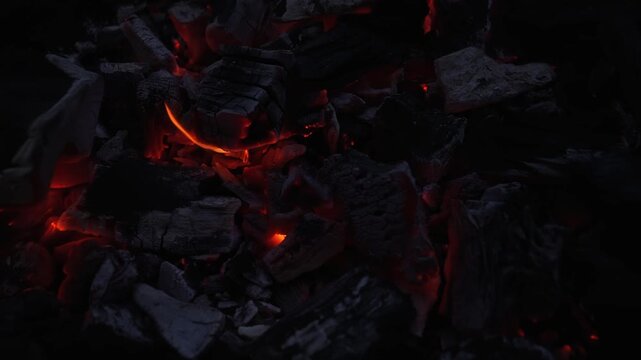 Close up of smoldering charcoal with glowing embers and ash texture in low light, ideal for fire, heat, grilling, fuel, and dramatic background concepts.