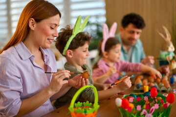 Mother painting easter egg with children at table