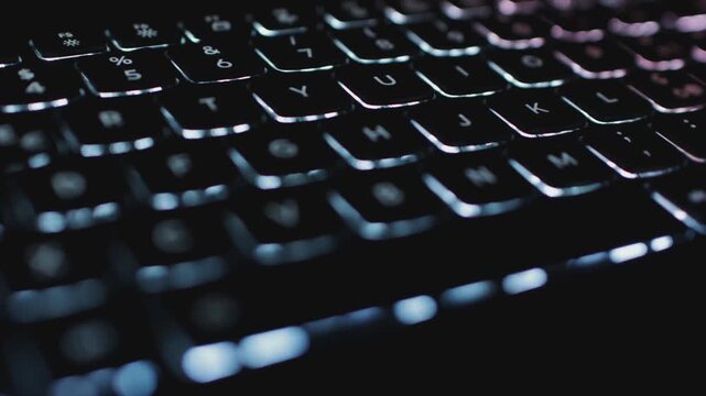 cinematic overview close-up of illuminated computer keyboard keys in low light with blue backlighting. Dolly macro shot of a laptop keyboard with backlight multicolors