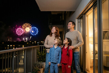 Obraz premium Family watching colorful fireworks from balcony at night 