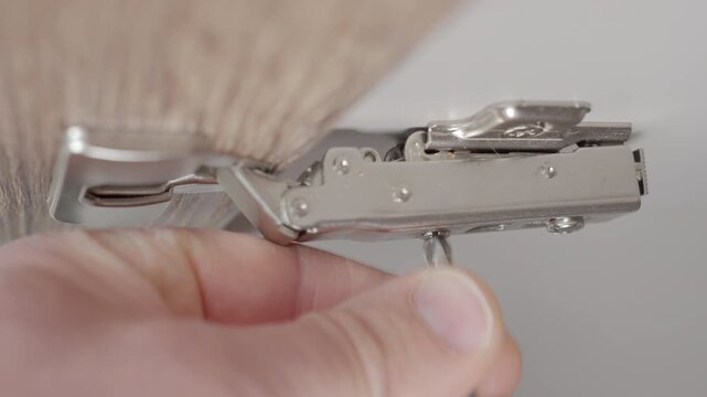 Hand adjusting metal cabinet door hinge using screwdriver inside wooden kitchen cabinet. Concept of home repair furniture installation and maintenance.