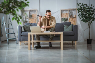 Fototapeta premium Man planning home renovation using laptop and smart phone