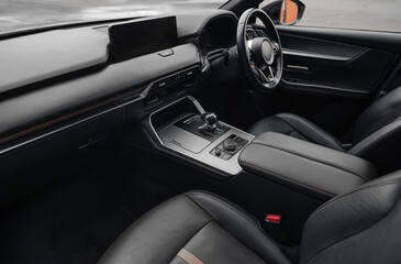 Right-hand drive luxury car interior with black leather. Car cockpit wide angle view from passenger side: seats, steering wheel, dashboard and center console.