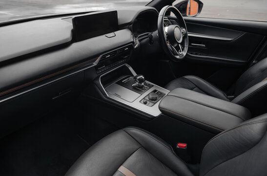 Right-hand drive luxury car interior with black leather. Car cockpit wide angle view from passenger side: seats, steering wheel, dashboard and center console.