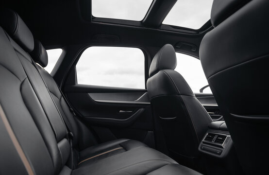 Rear row of seats in a car. SUV or wagon interior with black leather seats and panoramic glass roof, cloudy autumn sky in the background.