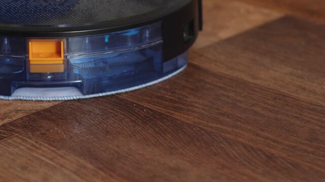 Robotic vacuum cleaner mopping the floor and navigating around furniture legs. Smart home device cleaning laminate with water tank and mop cloth