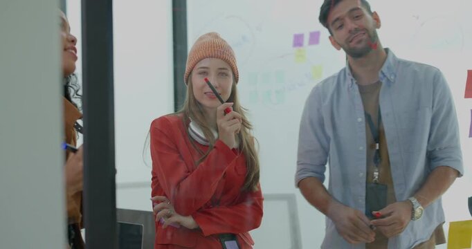 Diverse group of startup team engaging in brainstorming session, using sticky notes on glass wall to organize ideas, plan next steps. Creativity and collaborative spirit of modern entrepreneurial team