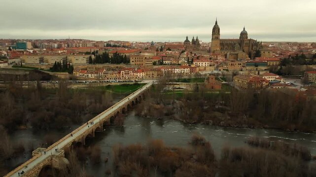 Aerial panoramic view of Salamanca featuring the cathedral complex and the Roman Bridge over the Tormes River. Historic architecture and skyline in western Spain.