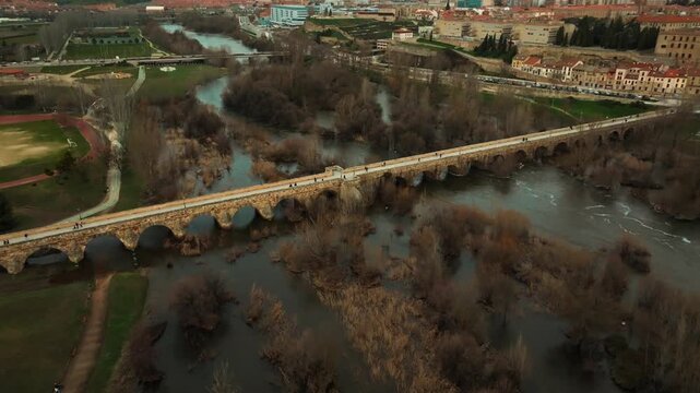 Drone aerial view of the ancient Roman stone bridge crossing the Tormes River in Salamanca, Spain. Historic landmark and architectural heritage captured from above.