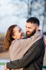 Naklejka premium Young couple embracing outdoors, smiling at each other with trees and a blurred natural background, wearing casual clothing in a relaxed setting