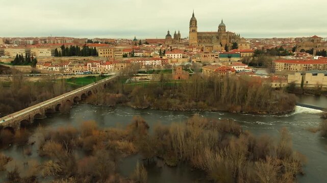 Aerial panoramic view of Salamanca featuring the cathedral complex and the Roman Bridge over the Tormes River. Historic architecture and skyline in western Spain.