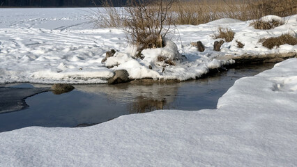 winter landscape with a flowing spring, the spring flows into a frozen lake, snow, sky, winter day