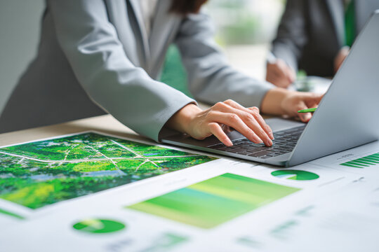 A person in business attire works on a laptop surrounded by green-themed charts and graphs, indicating data analysis or environmental planning.