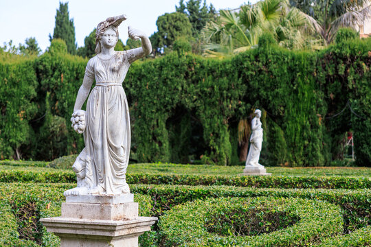 Eternal guardians of the labyrinth: classical female statues in a manicured boxwood garden (Guardianas eternas del laberinto: estatuas femeninas cl&aacute;sicas en un jard&iacute;n de boj perfectamente cuidado).