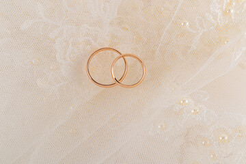 A pair of classic gold rings for the wedding ceremony lie on soft pleats of cream-colored veil with embroidery . A copy space. layout for design. postcard.