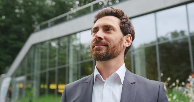 Close-up of a bearded businessman face, smiling confidently while looking to the side outdoors in an urban business environment. People and business concept