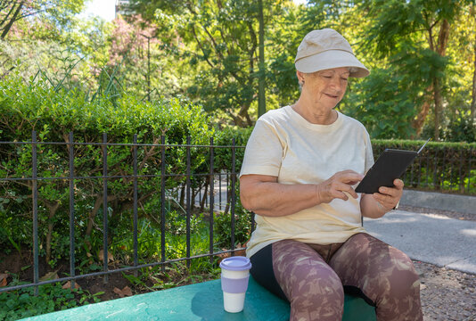 Senior white woman using an e-book reader in a park.
