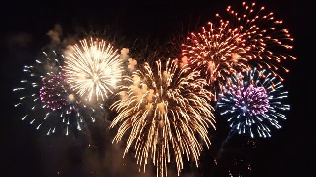Vibrant red and gold fireworks explode against a dark night sky, creating a dazzling display of light and color with smoky trails.