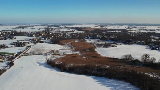 Winter aerial of rural town and snowy fields under blue sky, contryside landscape 4k.