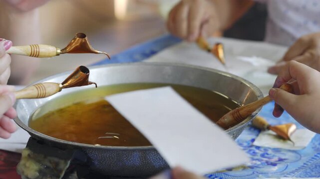 Close up of people using Tjanting tools to dip hot wax for traditional Batik making process.
