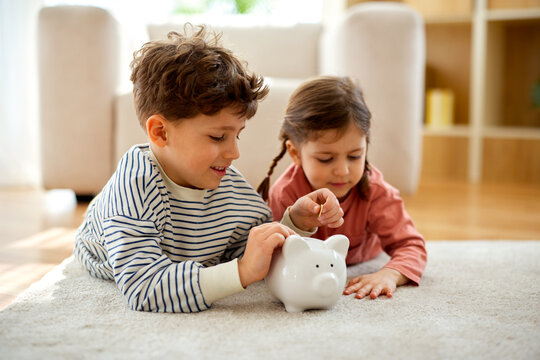 Children putting coins into piggy bank at home