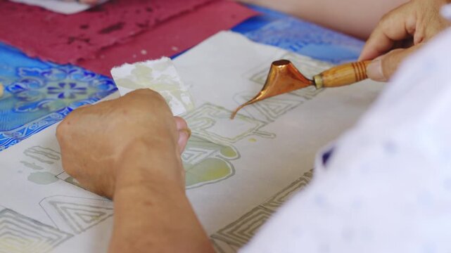 Close up of people using Tjanting tools to dip hot wax for traditional Batik making process.
