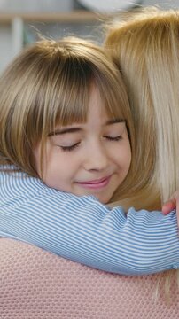 Attractive caring loving mother in pink sweater standing with her back to the camera and tenderly embracing her nice joyful teen daughter,warm family relations concept