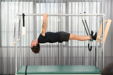 Sportswoman doing pilates aerial exercise on a trapeze table for flexibility and core training in fitness studio