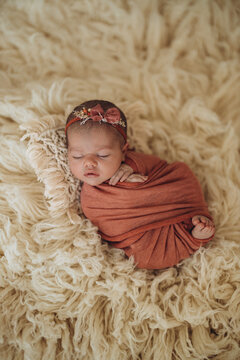 Newborn baby wrapped in soft fabric resting peacefully on fluffy textured rug