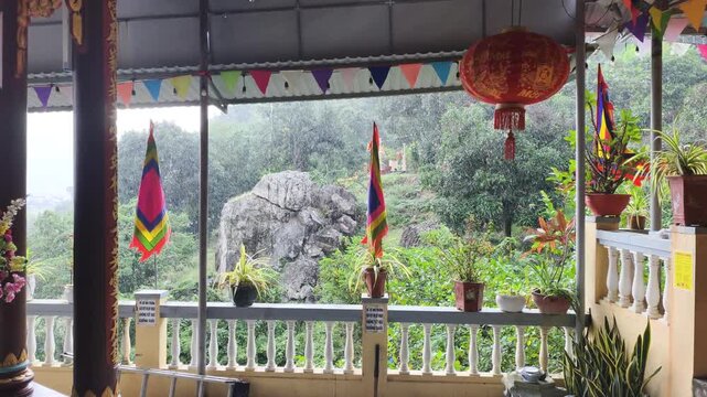 Wide view shows Spiritual Serenity in Rain with colorful flags waving near mountain pagoda. Heavy water drops fall during Spiritual Serenity in Rain amidst green misty jungle.