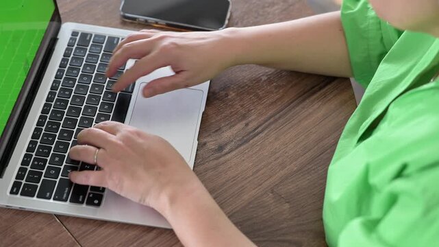 Woman typing on laptop at kitchen table while working from home. Freelance accounting and financial record-keeping concept.