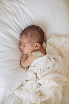 Newborn baby sleeping peacefully on soft white bedding in calm, serene indoor setting