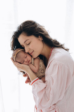 A mother gently holds her newborn baby close in a soft, warm embrace during quiet morning light.