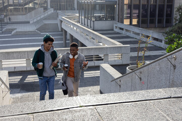Diverse male students walking up stairs on campus carrying paper cups and notebooks, copy space © wavebreak3