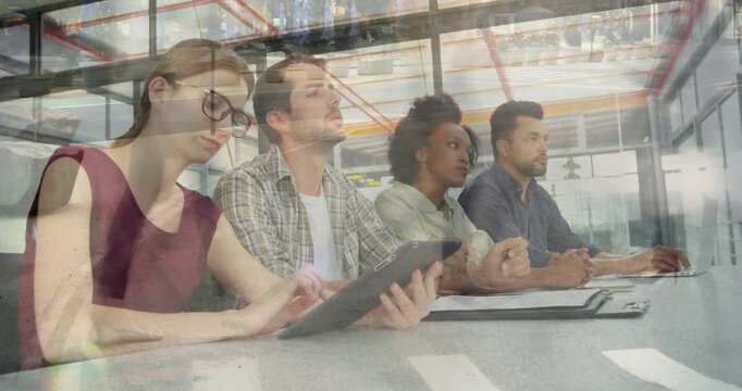 Team of four sitting in glass business meeting room, left woman tapping tablet initiating review