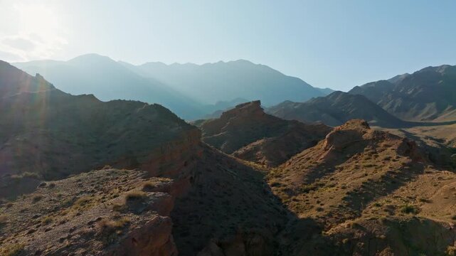 Vast mountain landscape captures arid terrain and dry shrubs under bright daytime sky. Serene natural beauty invites exploration and tranquility.