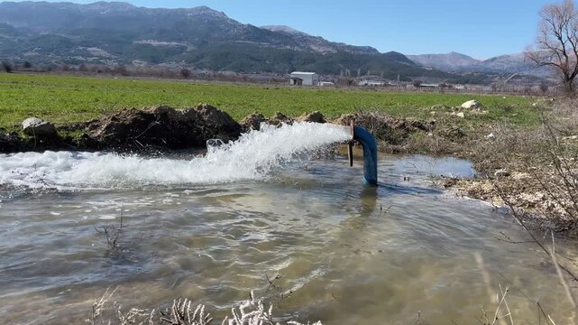 A natural flow created by water flowing under pressure from an agricultural irrigation pipe on a large plot of land with mountain views.
