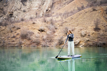 Naklejka premium Female on sup board in mountain lake in daylight. Water sport activity and healthy outdoor lifestyle in scenic environment. 