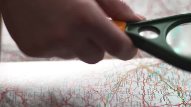 Hand holding magnifying glass over map for research and travel planning.