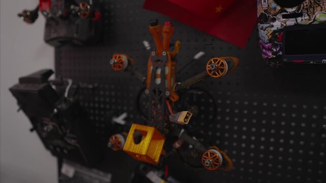 Fpv drone quadcopter resting on black pegboard displaying various racing components and accessories, representing the technical hobby of building and customizing remote controlled aircraft