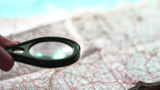 Hand holding magnifying glass over map for research and travel planning.